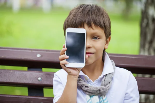Malý chlapec sedí na lavičce a volání do mobilních telefonů — Stock fotografie