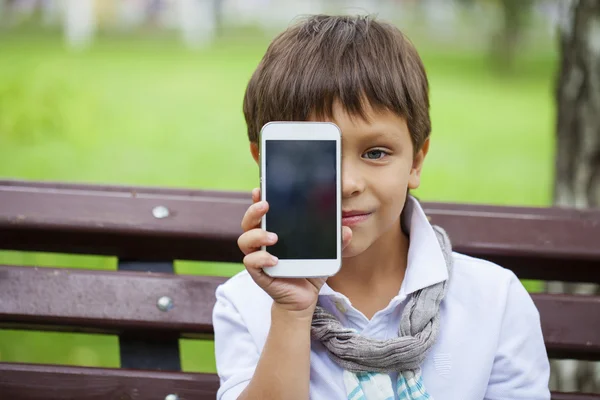 Malý chlapec sedí na lavičce a volání do mobilních telefonů — Stock fotografie