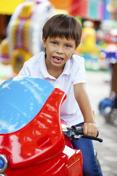 Маленький мальчик сидит на игрушечном мотоцикле в парке развлечений — стоковое фото