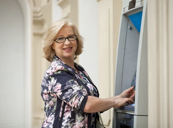 Femme blonde mature comptant l'argent près de guichet automatique — Photo
