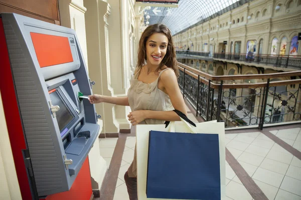 Mujer joven en pantalones vaqueros cortos usando un cajero automático — Foto de Stock