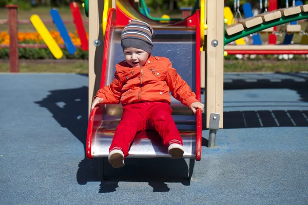 Blonde little boy sits on a childrens slide at the playground — Stock Photo, Image