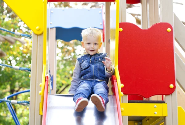 Blonder kleiner Junge sitzt auf Kinderrutsche auf Spielplatz — Stockfoto