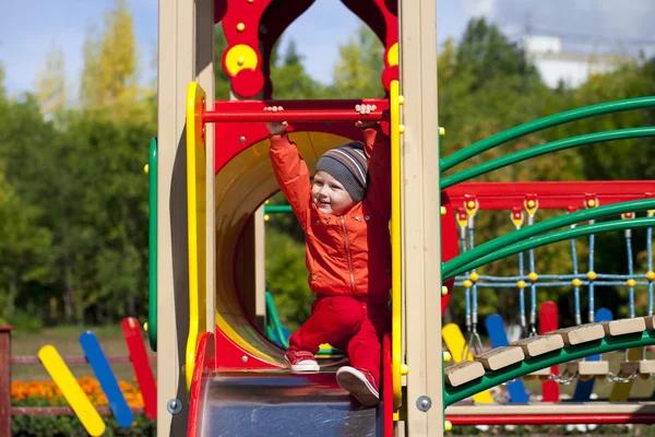 Menino loiro senta-se em um slide das crianças no parque infantil — Fotografia de Stock
