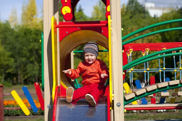 Menino loiro senta-se em um slide das crianças no parque infantil — Fotografia de Stock