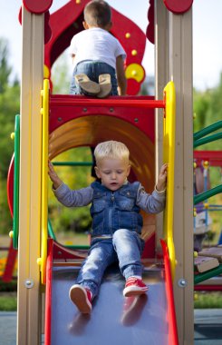 Sarışın küçük çocuk parkında bir çocuk slayt üzerinde oturur