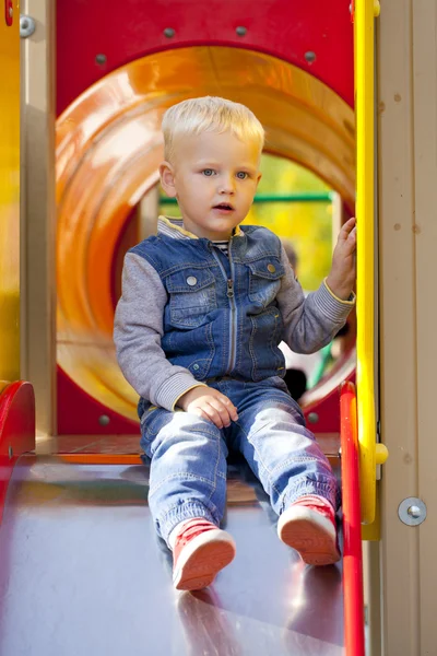 Blond liten pojke sitter på en barnens bild på lekplatsen — Stockfoto