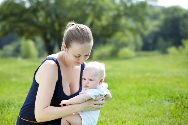 Mère attentionnée tient le bébé, contre le parc d'été — Photo
