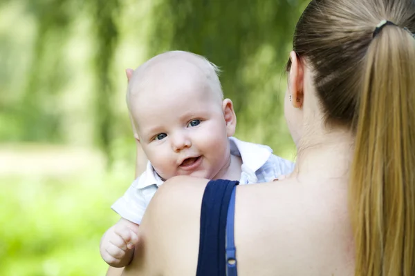 Mãe carinhosa está segurando o bebê, contra o parque de verão — Fotografia de Stock