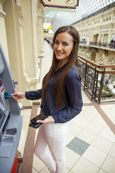 Wanita muda berambut cokelat yang bahagia menarik uang dari kartu kredit di — Stok Foto