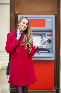 Sarışın genç kadın kırmızı paltolu geri çekmek para--dan bir Atm TH