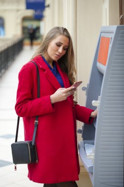 Sarışın genç kadın kırmızı paltolu geri çekmek para--dan bir Atm TH