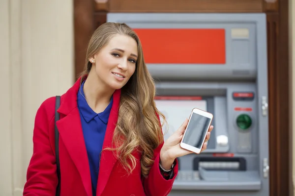Femme blonde en manteau rouge avec un téléphone à la main sur le dos — Photo