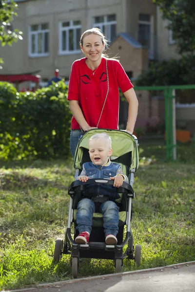 Een jongetje zit in een rolstoel en wandelen met zijn moeder — Stockfoto