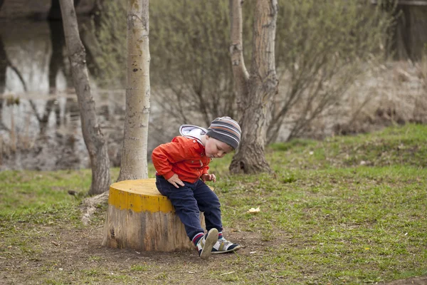 Little boy sitting on a stump in the spring park — Stock Photo, Image