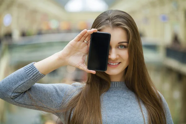 Mladá žena se vztahuje na její tvář obrazovka smartphone — Stock fotografie