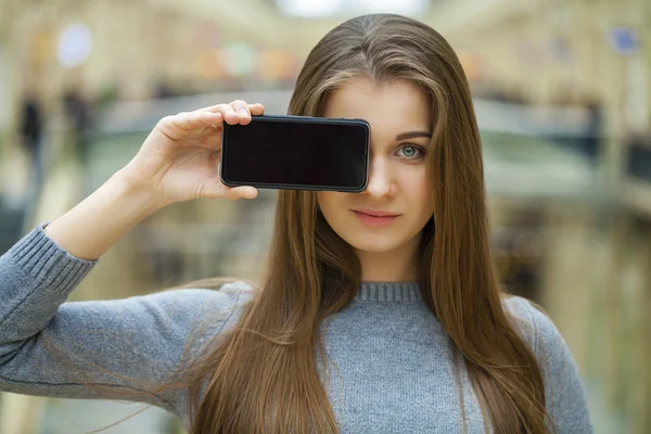 Mladá žena se vztahuje na její tvář obrazovka smartphone — Stock fotografie