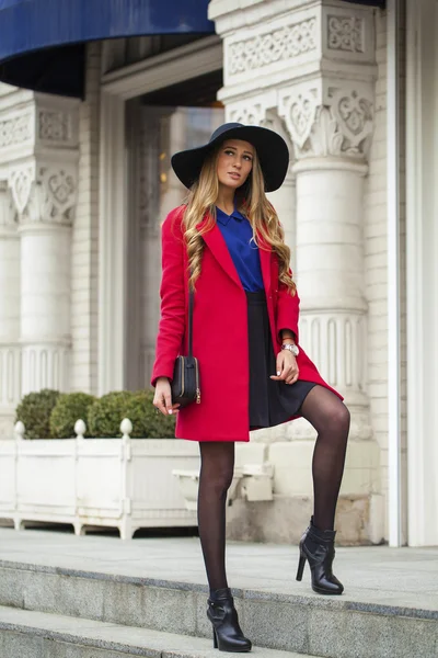 赤いコートを着た若い幸せな金髪女泉街の上を歩く — ストック写真