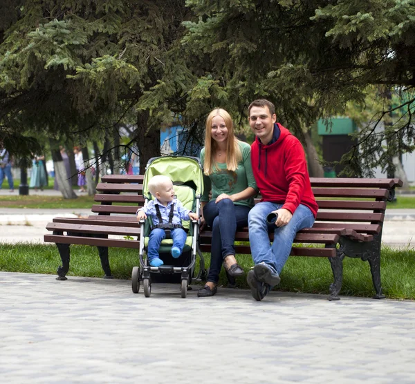 Giovani genitori si siedono su una panchina con il suo giovane figlio — Foto Stock