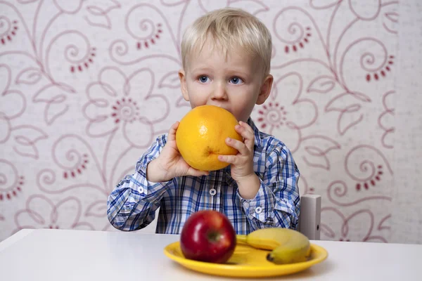 The three-year boy eats a yellow grapefruit — Stock Photo, Image