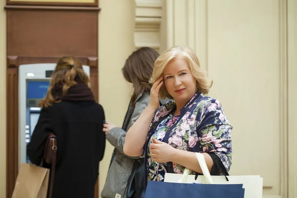 Reife blonde Frau mit Kreditkarte in der Hand in der Nähe des Geldautomaten — Stockfoto