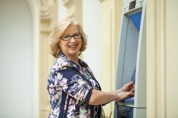 Mujer rubia madura con tarjeta de crédito en la mano cerca de cajero automático —  Fotos de Stock