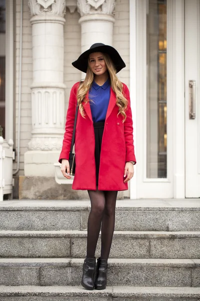 Молодая счастливая блондинка в красном пальто гуляет по весенней улице — стоковое фото
