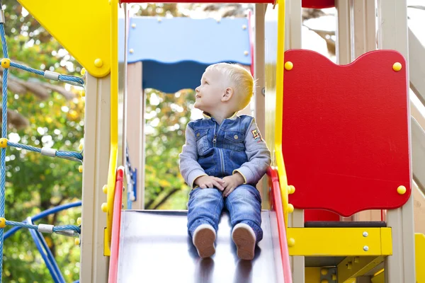 Blond liten pojke sitter på en barnens bild på lekplatsen — Stockfoto