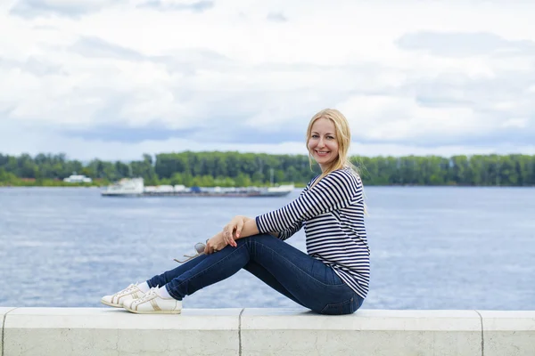 Young beautiful woman in blue jeans sitting in summer street par — Stock Photo, Image