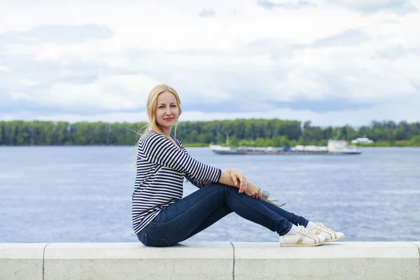 Young beautiful woman in blue jeans sitting in summer street par — Stock Photo, Image