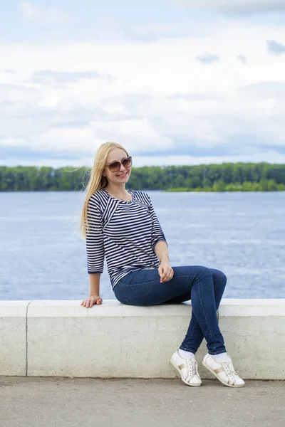 Young beautiful woman in blue jeans sitting in summer street par