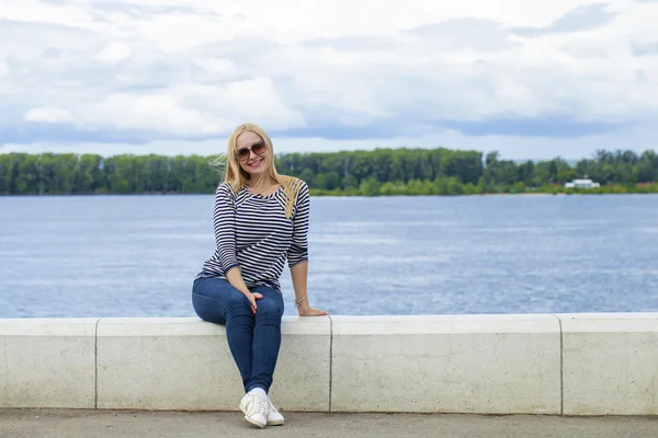 Young beautiful woman in blue jeans sitting in summer street par — Stock Photo, Image