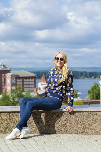 Молодая красивая женщина в синих джинсах, сидящая на летней улице — стоковое фото