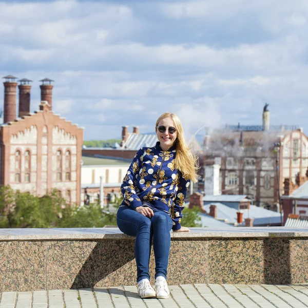 Young beautiful woman in blue jeans sitting in summer street par — Stock Photo, Image