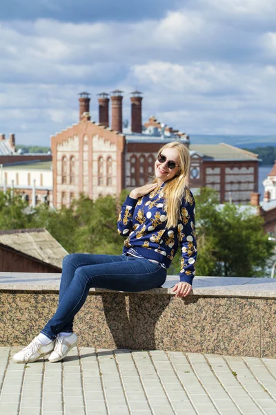 Young beautiful woman in blue jeans sitting in summer street par — Stock Photo, Image