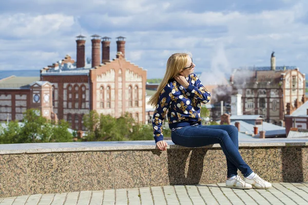 Young beautiful woman in blue jeans sitting in summer street par — Stock Photo, Image