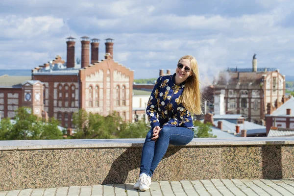 Young beautiful woman in blue jeans sitting in summer street par — Stock Photo, Image