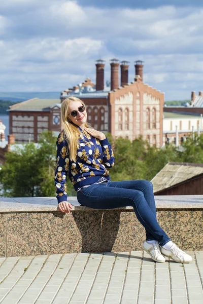 Joven hermosa mujer en pantalones vaqueros azules sentado en la calle de verano par —  Fotos de Stock