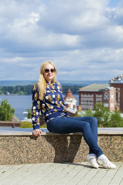 Young beautiful woman in blue jeans sitting in summer street par — Stock Photo, Image