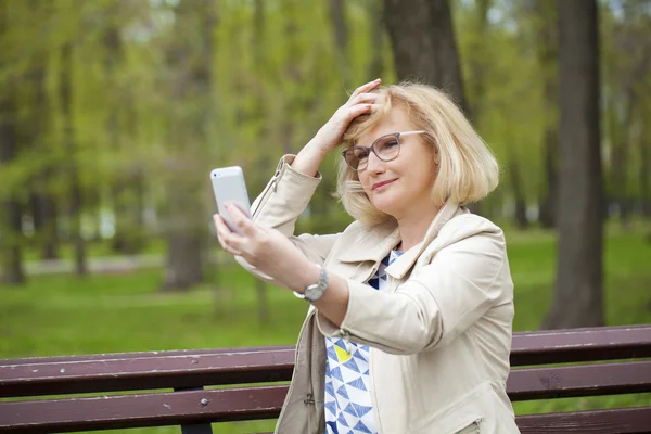 Mature beautiful woman reads the message on the phone — Stock Photo, Image