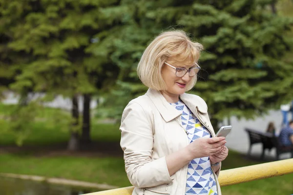 Mature beautiful woman reads the message on the phone — Stock Photo, Image