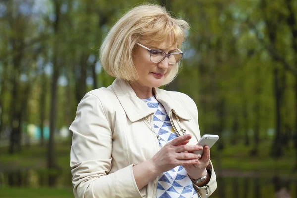 Mooie rijpe vrouw leest het bericht op de telefoon — Stockfoto