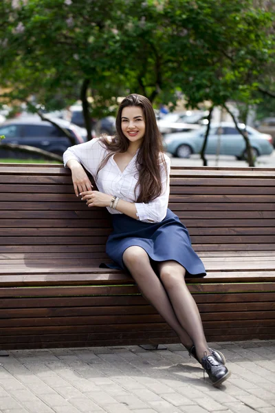 Jovem menina bonita sentada em um banco no parque de verão — Fotografia de Stock