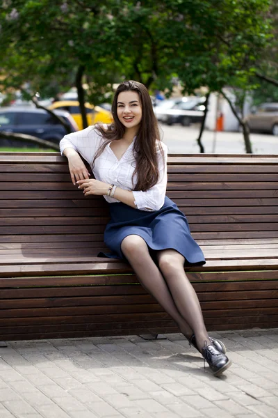 Молодая красивая девушка сидит на скамейке в летнем парке — стоковое фото