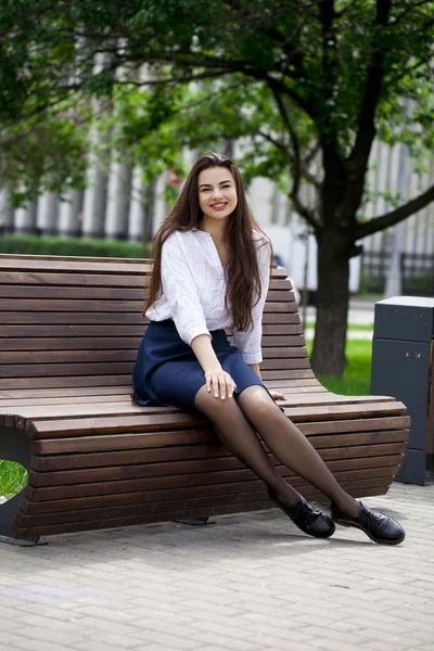 Jovem menina bonita sentada em um banco no parque de verão — Fotografia de Stock