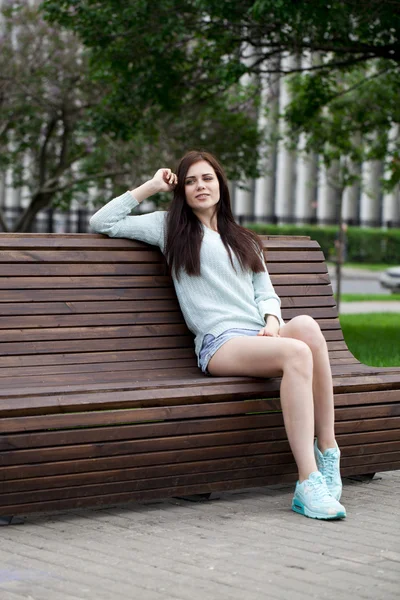 Jovem menina bonita sentada em um banco no parque de verão — Fotografia de Stock