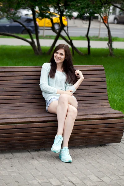 Jovem menina bonita sentada em um banco no parque de verão — Fotografia de Stock