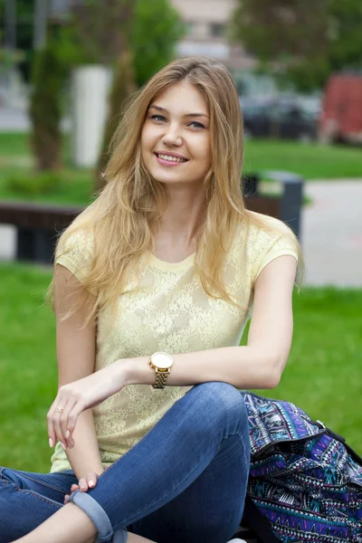 Jovem menina bonita sentada em um banco no parque de verão — Fotografia de Stock