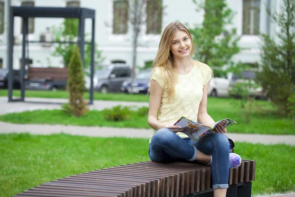 Jovem menina bonita sentada em um banco no parque de verão — Fotografia de Stock