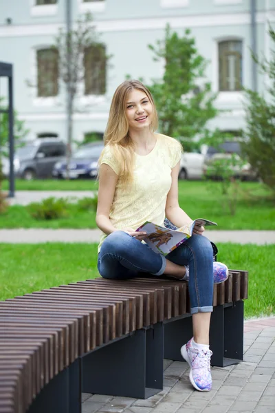 Jovem menina bonita sentada em um banco no parque de verão — Fotografia de Stock